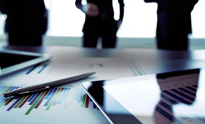 Image of a laptop on a desk with graphs and documents surrounding it